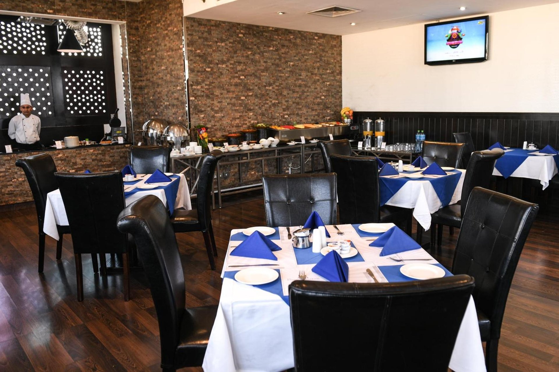 a dining room with tables and chairs with blue napkins at Juffair Grand Hotel in Manama