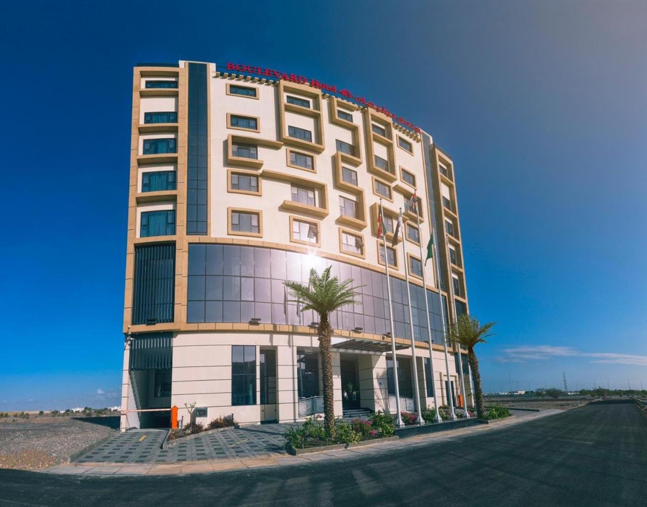 a tall building with palm trees in front of it at Boulevard Oman Hotel in Muscat
