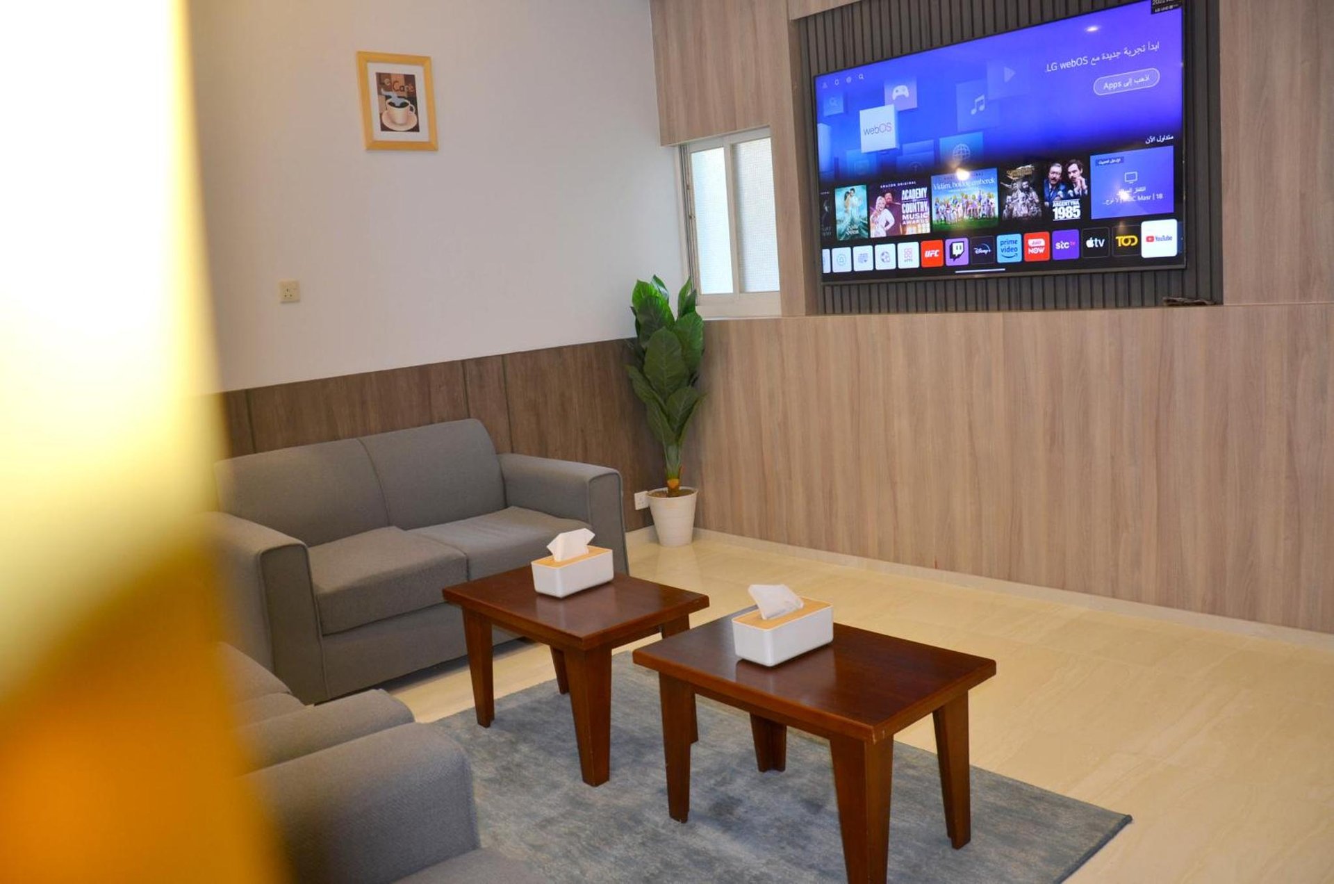 Living area with wall-mounted smart TV (YouTube, Netflix, apps), gray sofa, two wooden coffee tables and tissue box at فندق فربيون ابها - Ferbion Hotel Abha in Abha