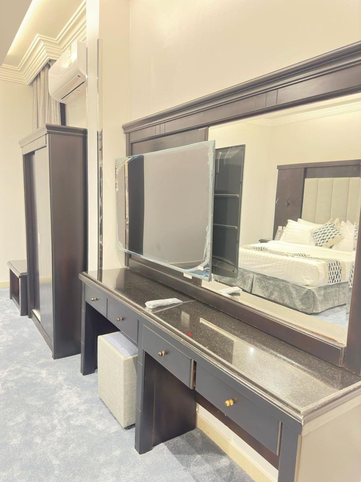 Guest room with wall-mounted TV, large mirror, dark wood dresser with drawers and ottoman, wardrobe and air conditioner at فربيون للشقق الفندقية ابها-ferbion hotel apartment in Abha
