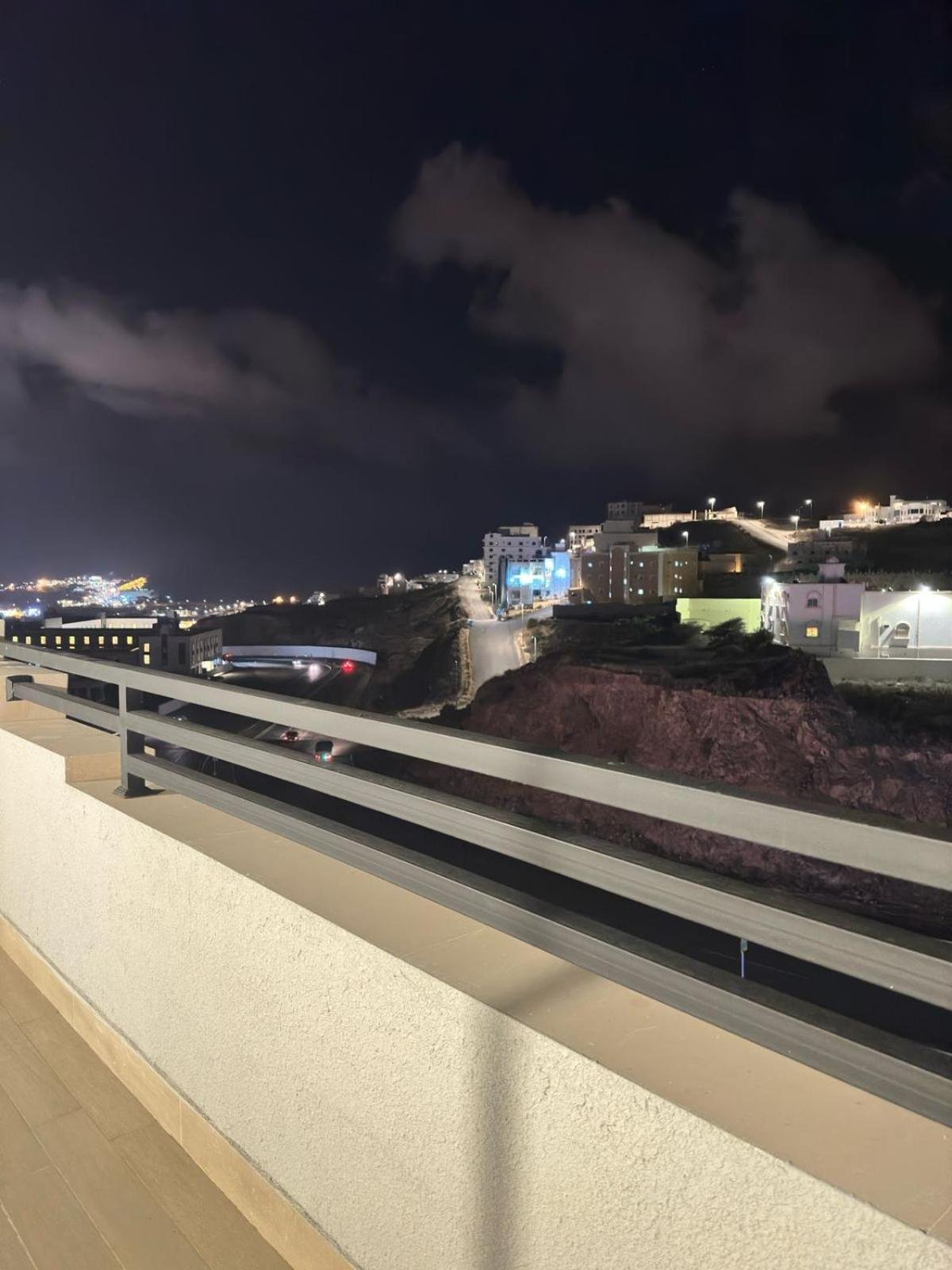 Balcony view at night over a coastal town with hillside buildings, lit harbor cranes and a winding road to the town at فربيون للشقق الفندقية ابها-ferbion hotel apartment in Abha