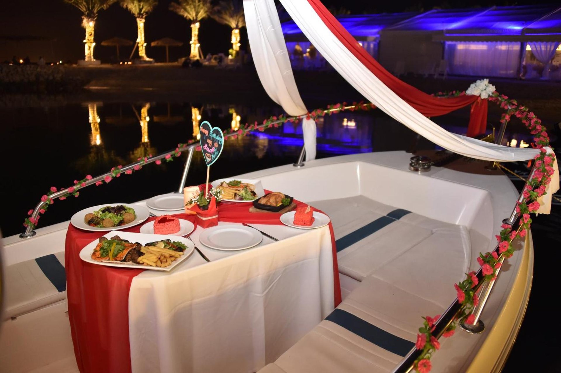 Waterfront boat dining with red draped canopy, floral garlands, four place settings and a 'Happy Birthday' heart at Lagoona Beach Luxury Resort and Spa in Al Budayyiâ€˜ +151 photos
