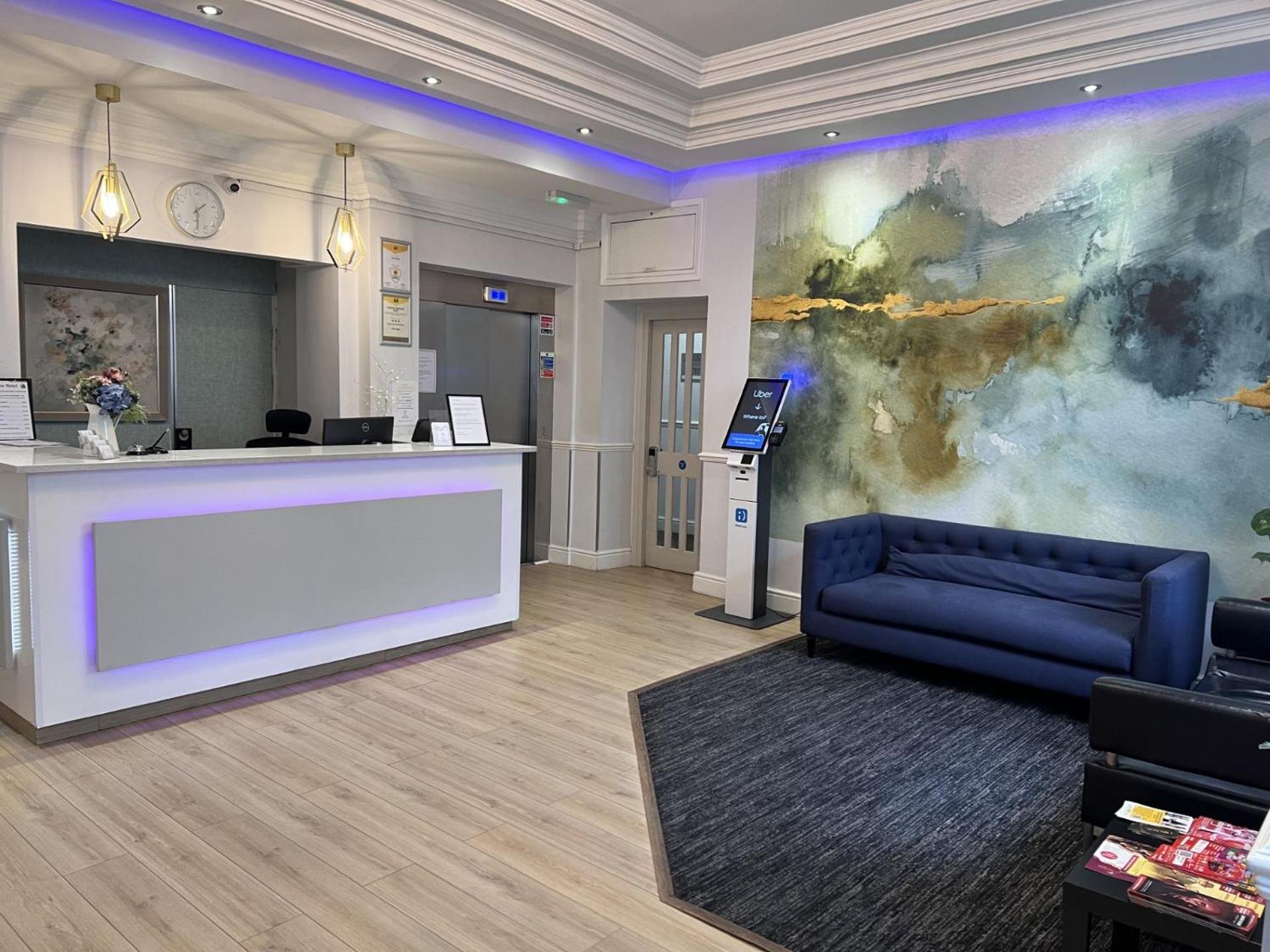 a lobby with a blue couch and a painting on the wall at Lidos Hotel in London